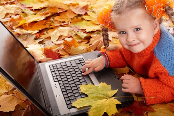 Girl child in autumn orange leaves with laptop.