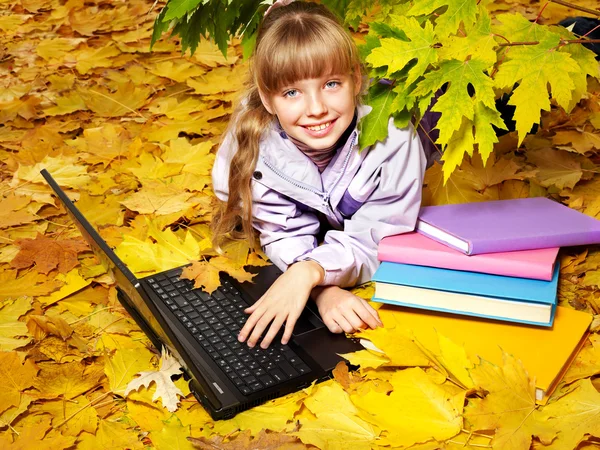 Kid in autumn orange leaves with laptop.