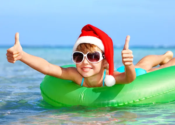 Child in santa hat floating on inflatable ring in sea.