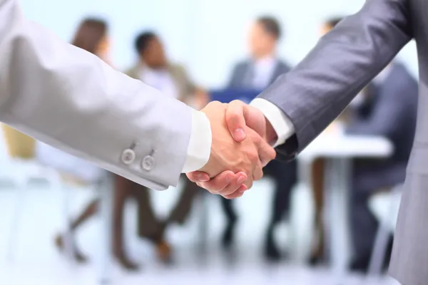 Two successful businessman shaking hands in front of corporate team at offi