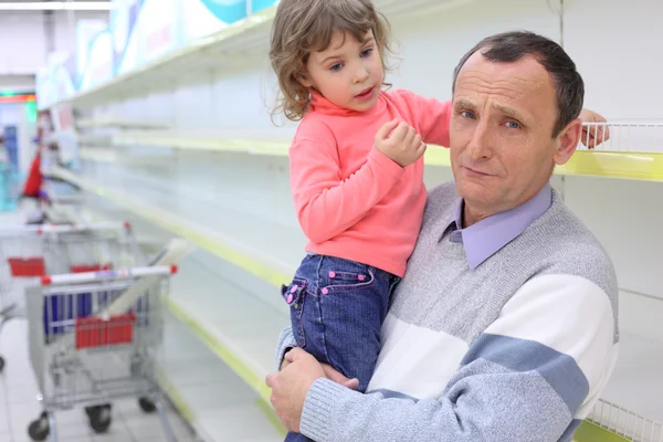 Elderly man at empty shelves in shop with child on hands