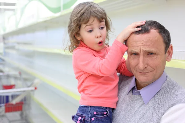 Elderly man at empty shelves in shop with child on hands