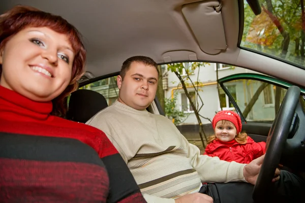 Married couple and little girl sit in car near a building