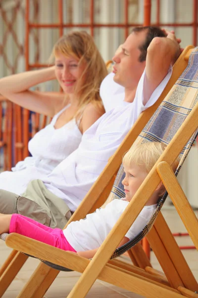 Happy family with little girl reclining on chaise lounges on ver