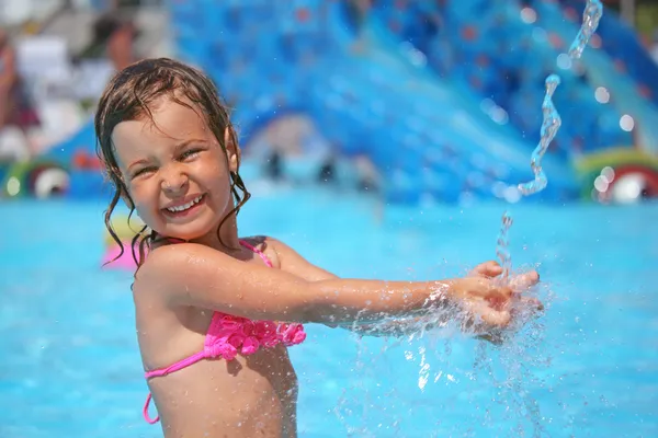 Little girl bathes in pool under water splashes in aquapark