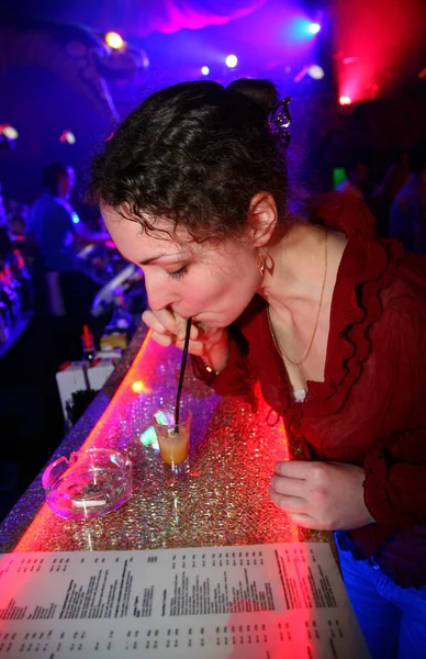Young curly woman drinking hot small drink in night club and watch menu to