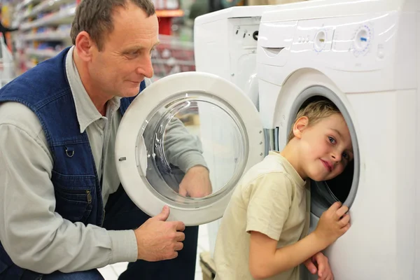 Man looks at washing machine in store, boy glances inward it