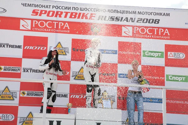 Girls-motorcyclists on pedestal with champagne
