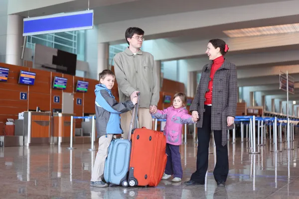Family with boy and girl standing in airport hall with two suitc