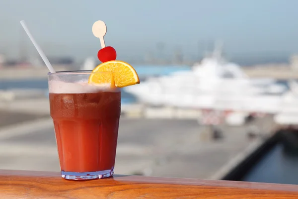 Cocktail with fruits in glass on ship deck rail, port with cruis