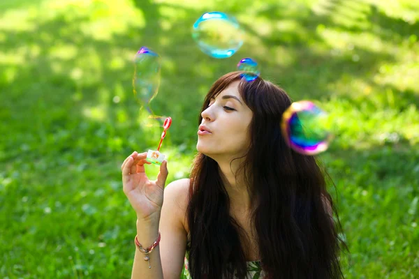 Portrait of attractive young girl inflating colorful soap bubble