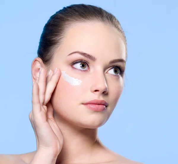 Woman applying cream on skin around her eyes