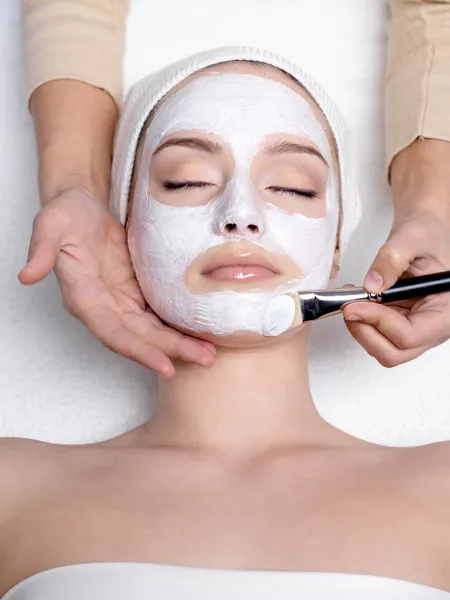 Cosmetician apllying healthy mask on face of young woman