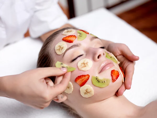 Woman receiving fruit facial mask at spa salon