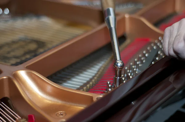 Piano with open cap. Human hand and tuning instrument