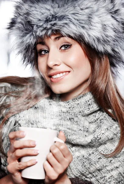 Girl blowing on hot drink dressed in winter clothing