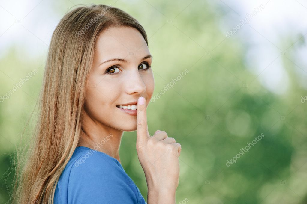 Beautiful young girl holding his index finger around lips and called for
