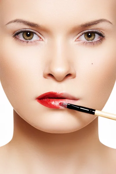 Close-up frontal portrait of beautiful woman model applying lipstick