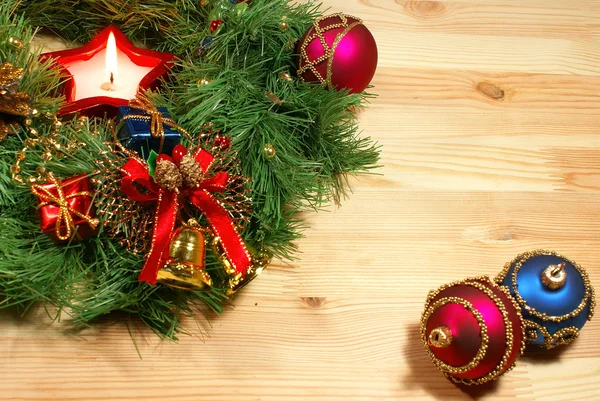 Nice Xmas decorations: red and blue spheres, golden bells, red candle and Xmas wreath over wooden desk