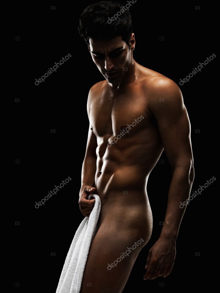 Young naked athlete standing with a towel against black background