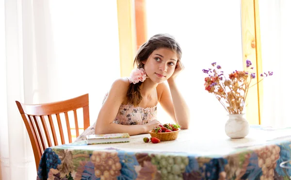 Pensive girl with book sitting at table indoor in summer day wit