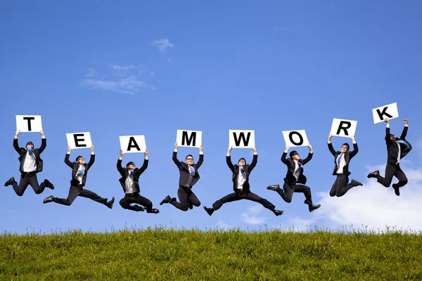 Happy businessman holding teamwork text and jumping on the green field