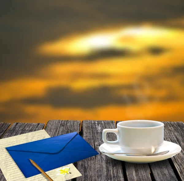 Coffee cup and letter on the wooden table with sunset sky background