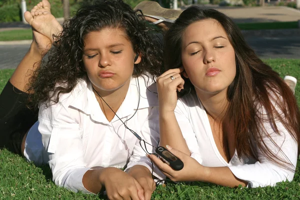 Teens students relaxing on campus listening to music sharing earphones and