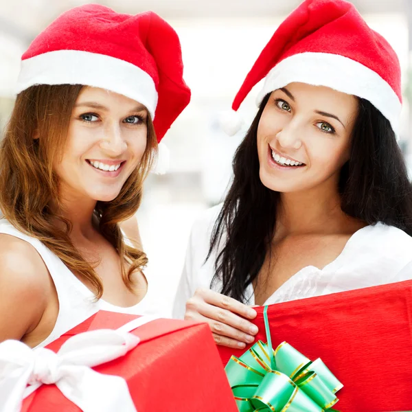 Young happy girls in Christmas hats.Standing together indoors and holding b