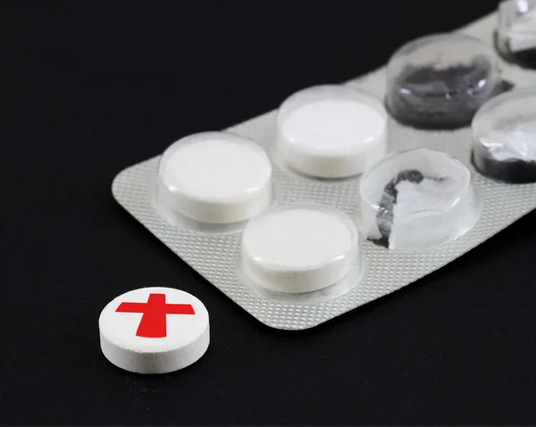 White pills with red cross in a black background