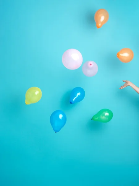 Hand releasing colorful balloons on blue background