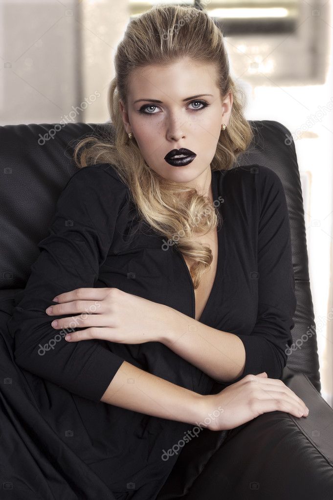 Fashion shot of a sophisticated blonde sitting on a black sofa wearing a