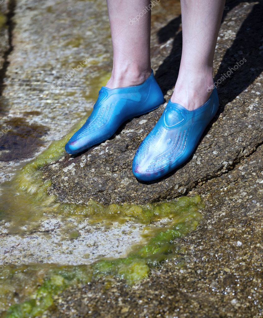 Closeup of a young woman's feet wearing swim shoes while on a rocky beach