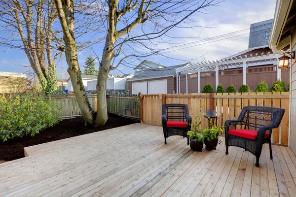 Deck with two chairs and fenced yard near home exterior shot.