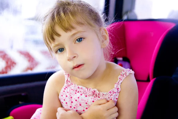 Blond child girl sitting in car safety seat