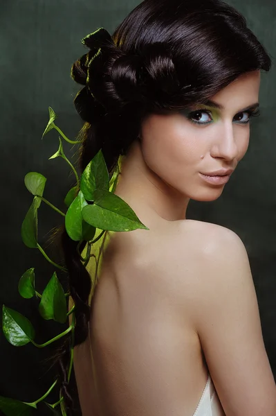 Beautiful young woman with green make up and some leaf in her long hair