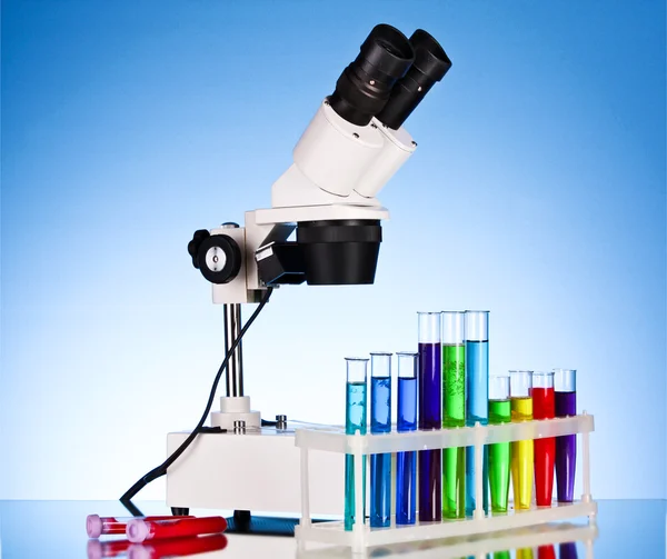 Laboratory metal microscope and test tubes with liquid on blue b