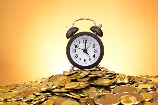 Alarm clock and coins on yellow background