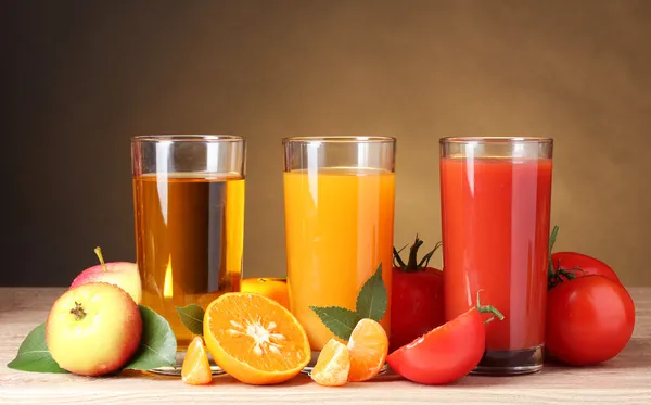 Different juices and fruits on wooden table on brown background