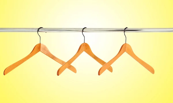 Wooden coat hangers on a clothes rail over yellow background