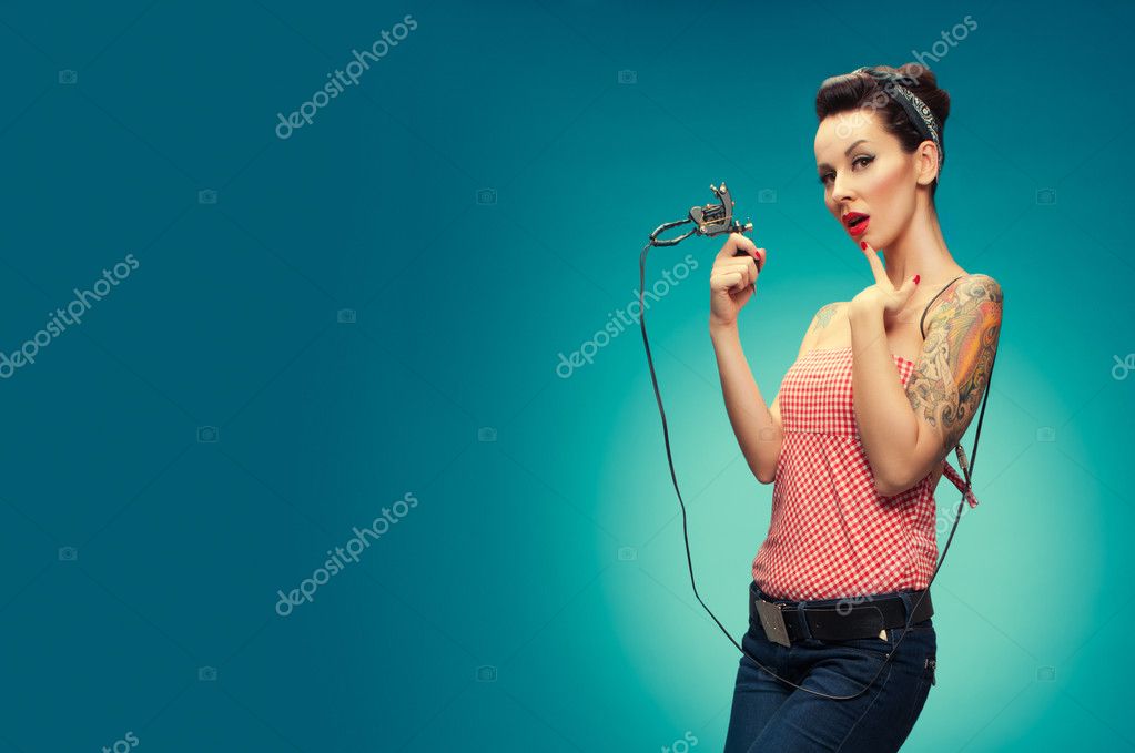 Photo of the sexy pin up girl with tattoos holding a tattoo machine