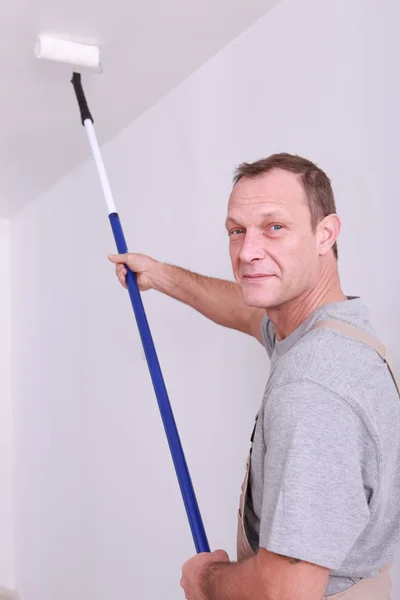 Decorator using a long roller to paint a ceiling