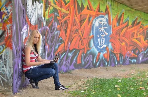 Girl against a wall with graffiti and laptop
