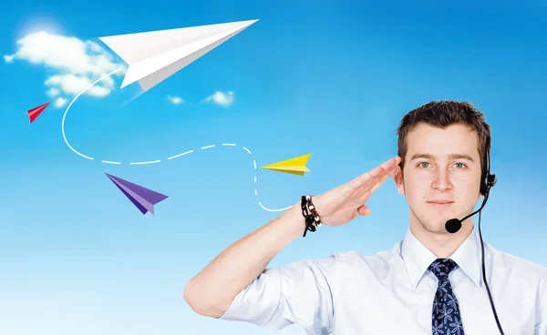 Young man salutes against the blue sky with a paper airplanes