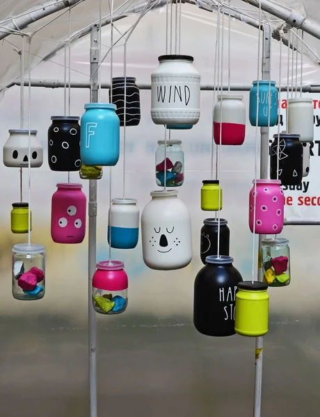 Glass jars, painted with different colors hanging on the ropes a