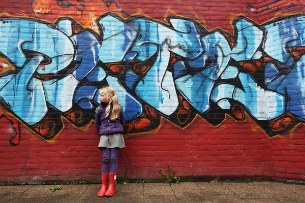 Little girl in front of a brick wall with graffiti