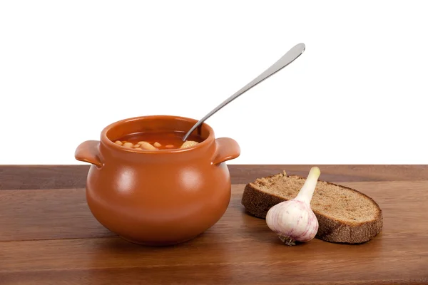Borsch in clay pot with bread and garlic on wooden table — Stock Photo, Image