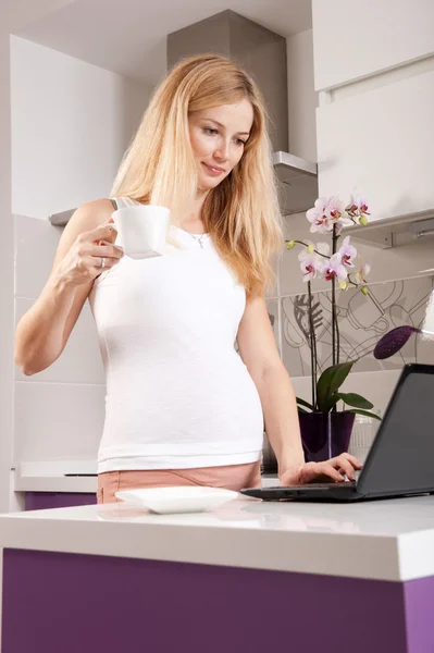 Mujer embarazada con portátil en la cocina — Foto de Stock