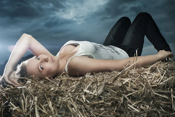 Menina bonita deitada no céu tempestuoso palheiro no fundo — Fotografia de Stock