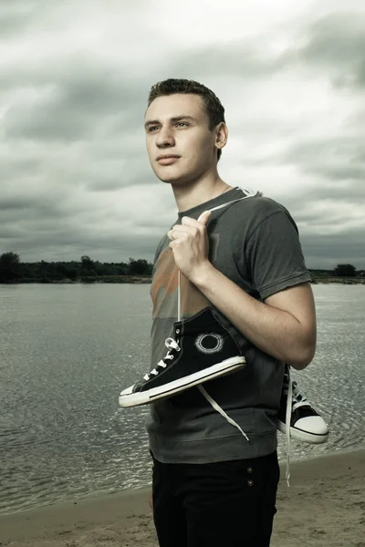 Portrait of young man standing on the river bank with trainers — Stock Photo, Image